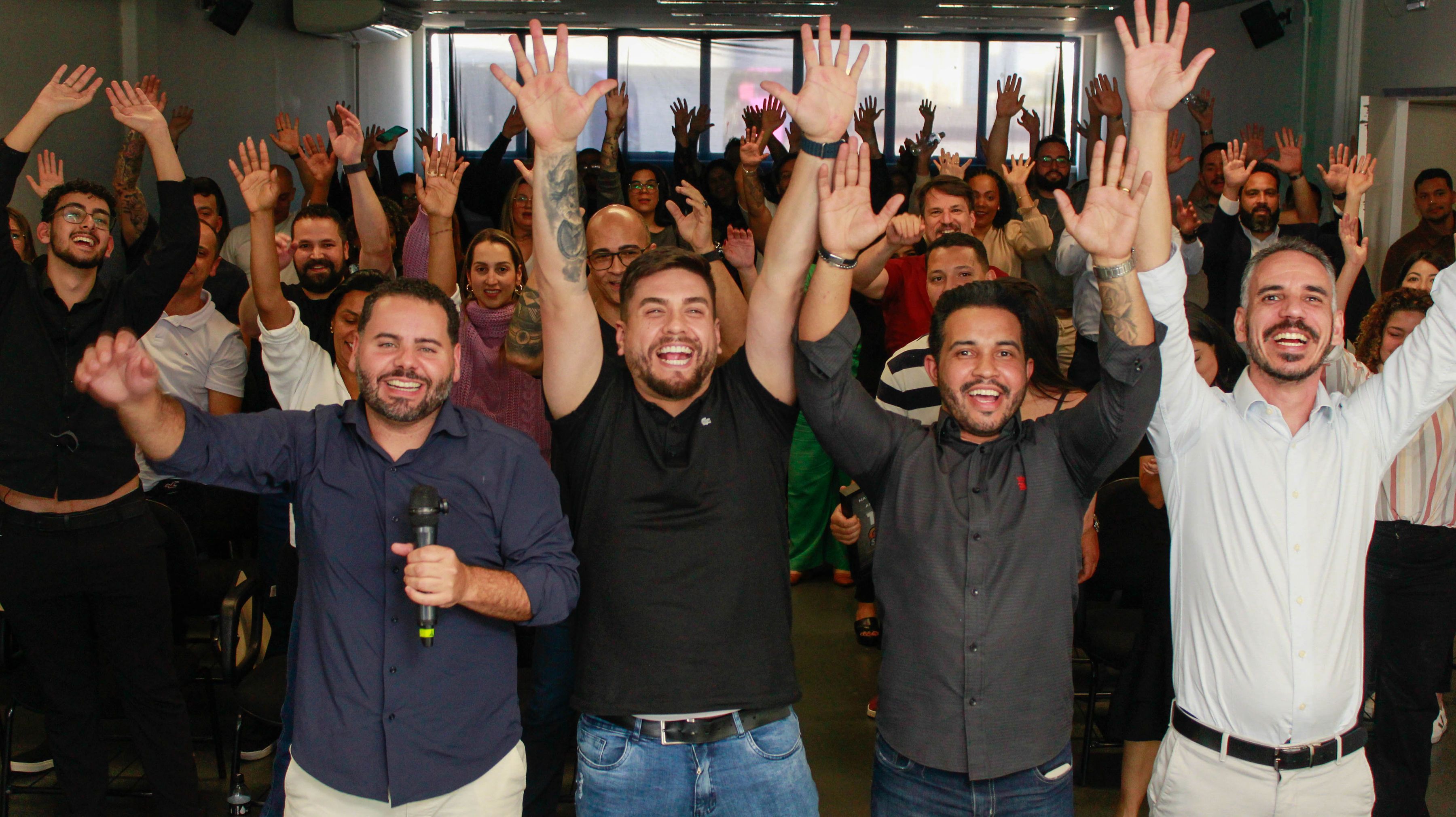 Participantes com as mãos para cima e o Léo ao microfone.
